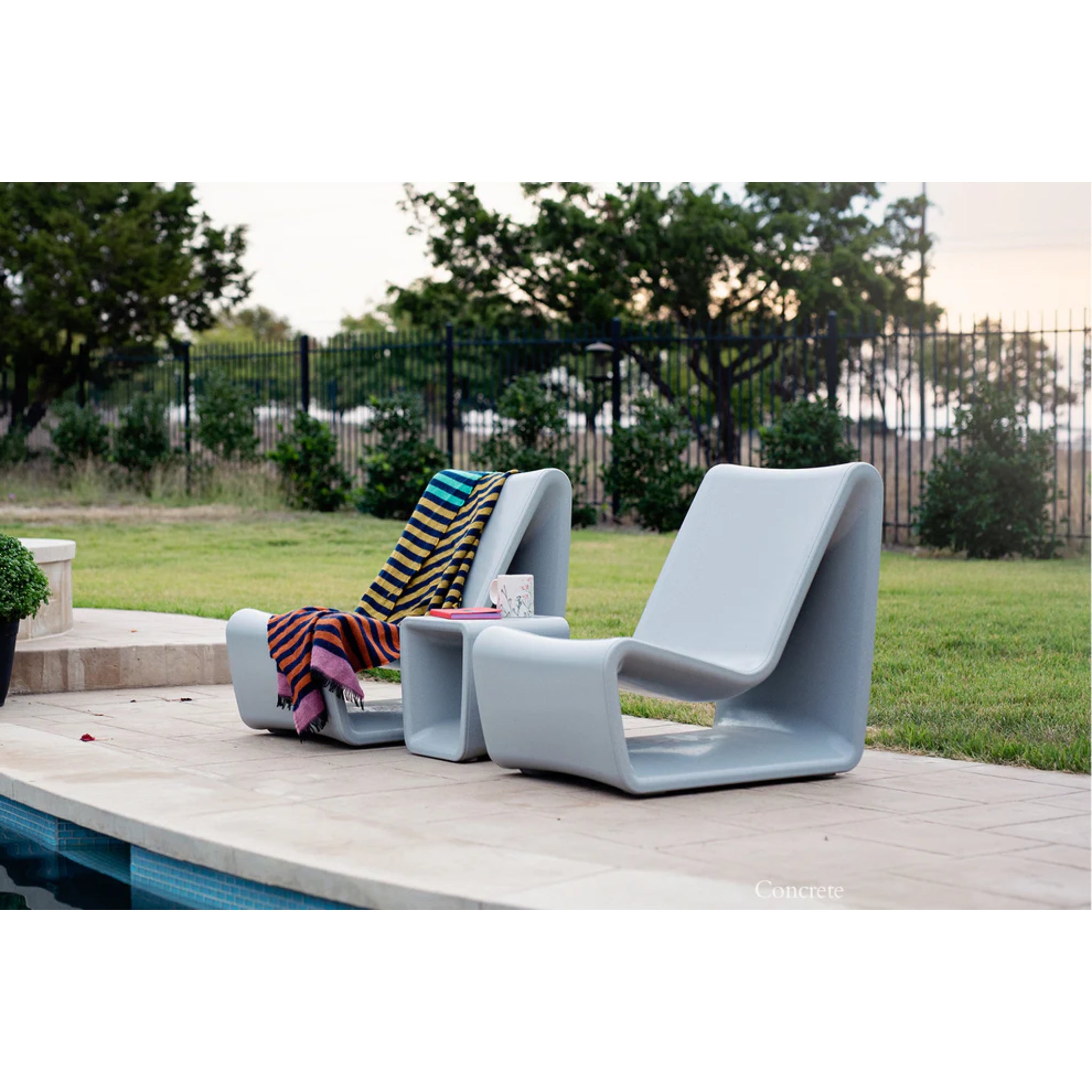 Concrete gray outdoor lounge chair positioned beside a luxury swimming pool and tanning ledge
