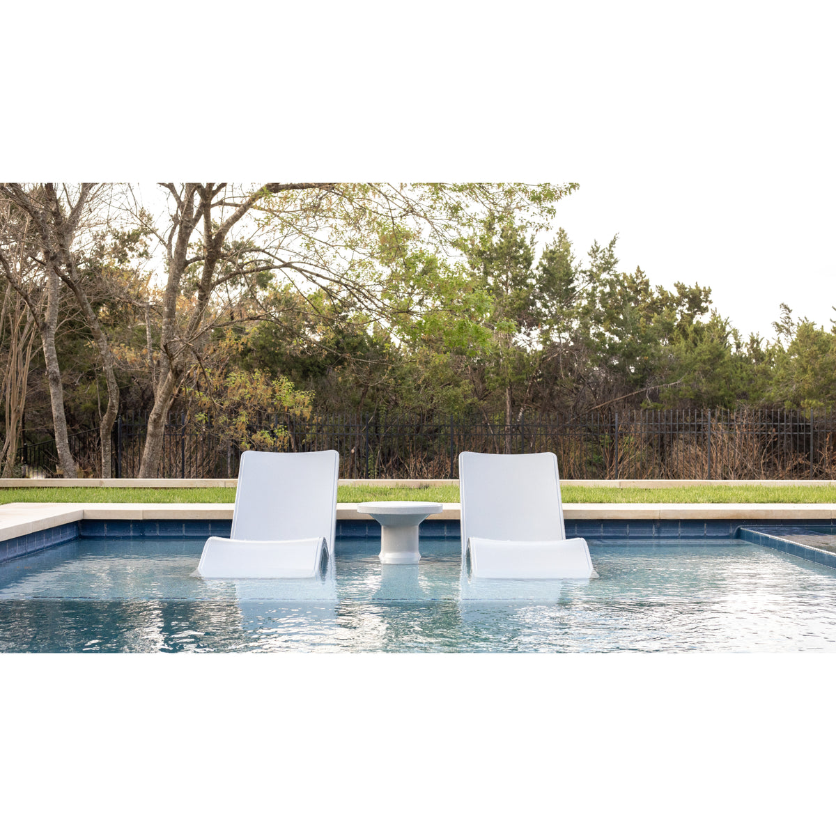 Pair of white baja shelf pool lounge chairs on a sun shelf surrounded by dense greenery and trees, water lapping at the base of each chair, SKU 8902-700 in Highcloud White.