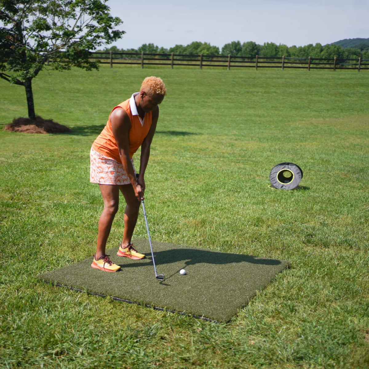 Golfer using the Real Feel Country Club First Cut 5' x 5' golf practice mat outdoors to practice controlled chip shots toward a portable target, demonstrating realistic first-cut turf resistance for backyard short-game training.