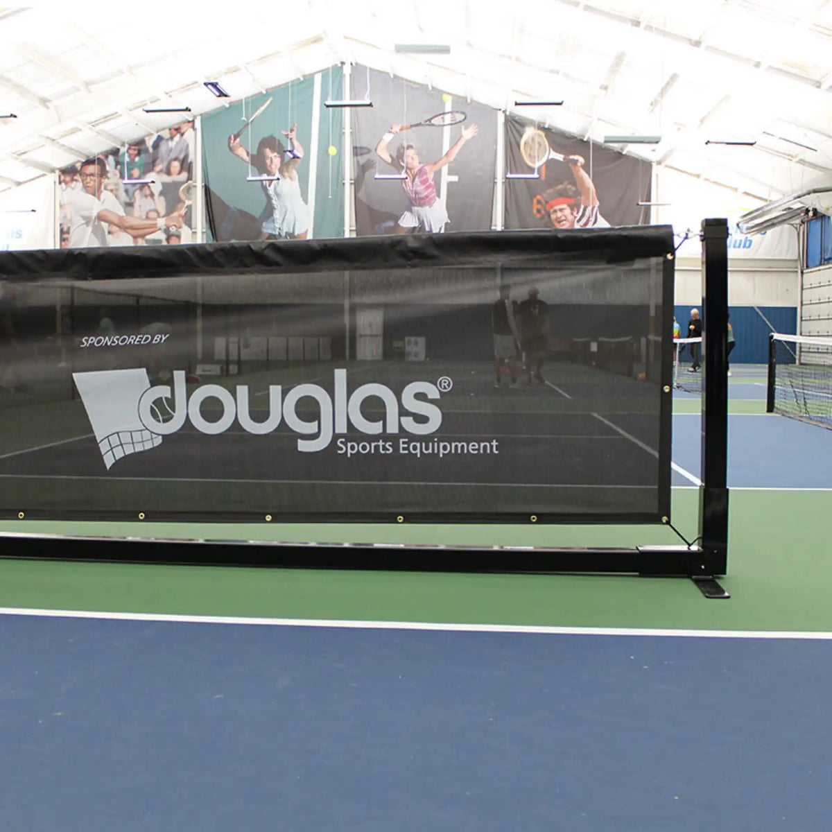Douglas pickleball court divider barrier installed in an indoor sports facility with black mesh panel and freestanding steel frame.