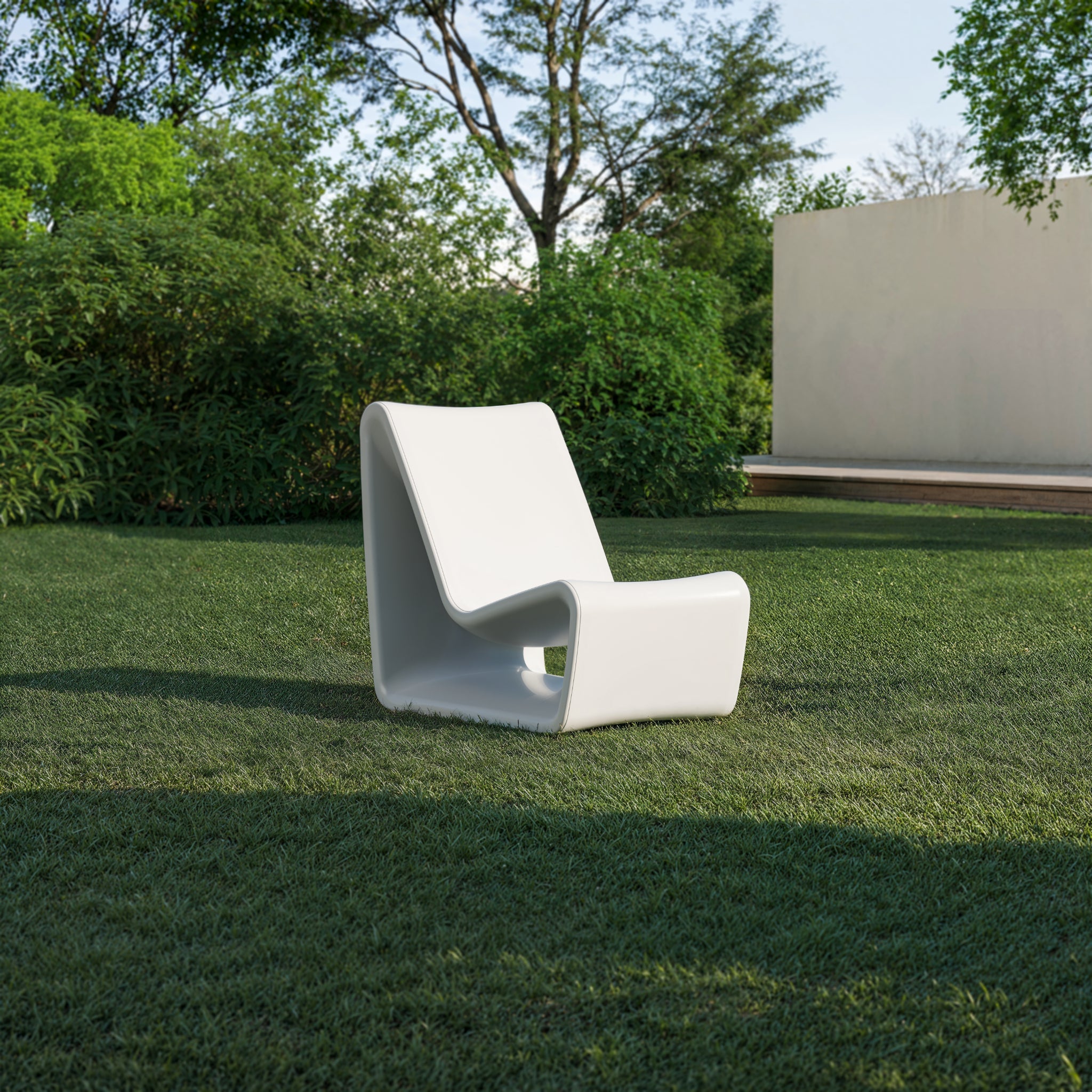 A modern Loop Lounge chair in Highcloud White sitting on a lush green lawn, highlighting its sculptural design in a contemporary outdoor backyard setting.