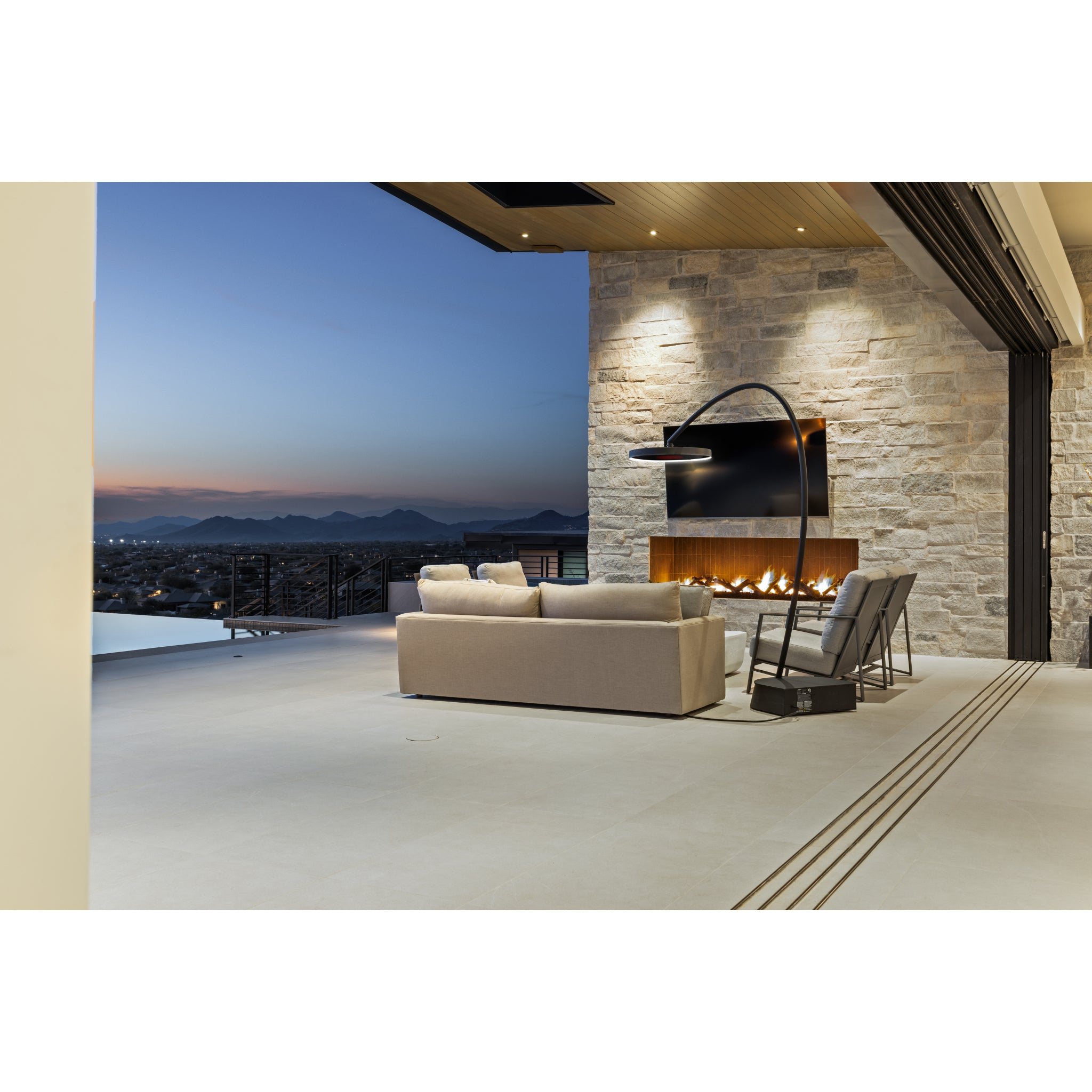 Modern outdoor living space with a sofa, chairs, and fireplace overlooking a scenic view with Bromic patio heater