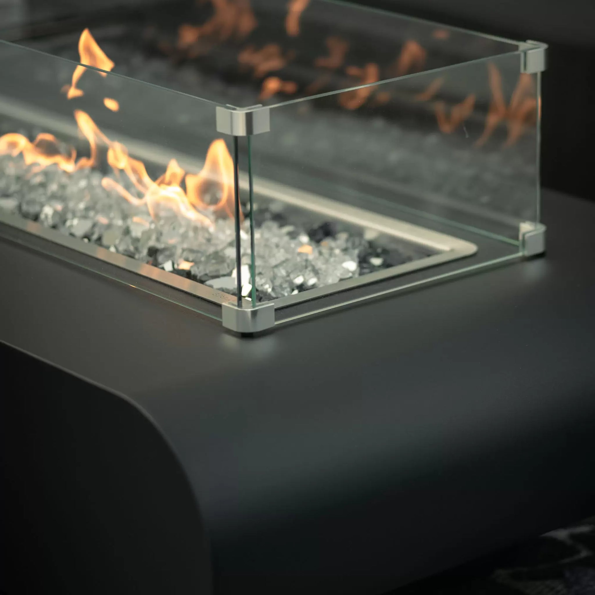 The Outdoor Plus tempered glass wind guard installed on a luxury outdoor fire pit with polished chrome connectors