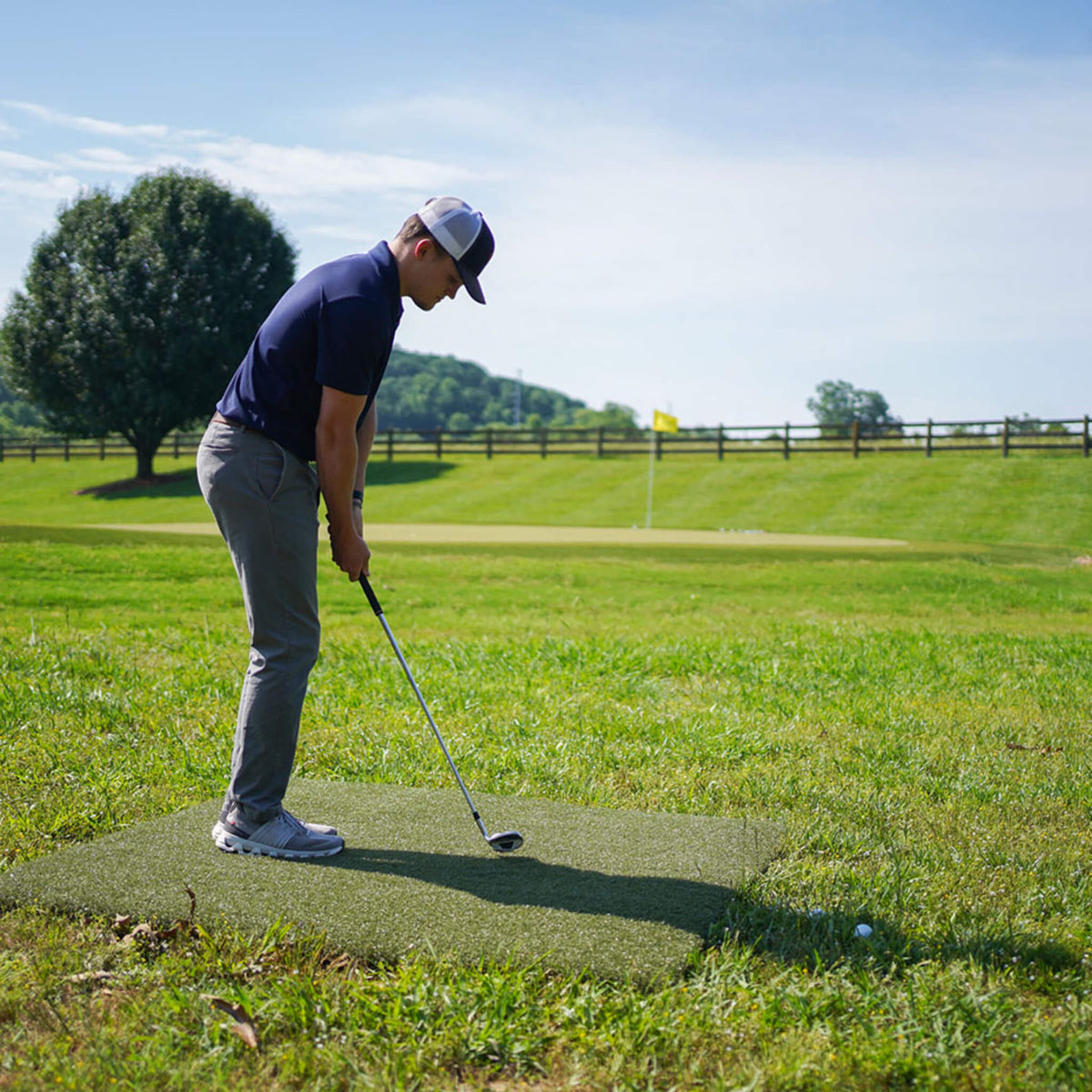 Golfer hitting an approach shot from a 5' x 5' Real Feel Country Club First Cut golf practice mat, designed to simulate first-cut fairway turf for realistic chipping, pitching, trajectory control, and backyard short-game practice.