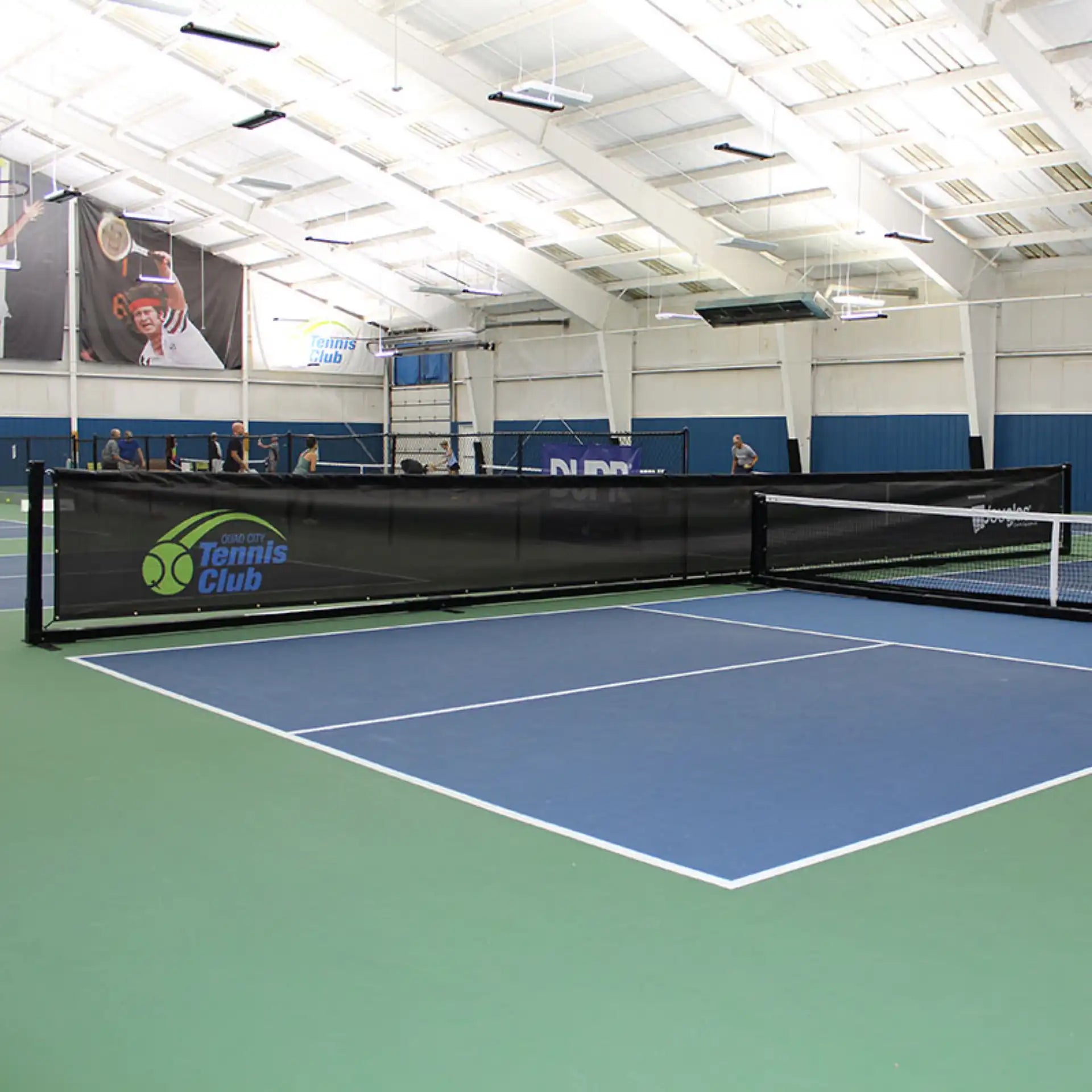 Douglas movable pickleball court divider system separating indoor pickleball courts with a freestanding black mesh barrier.