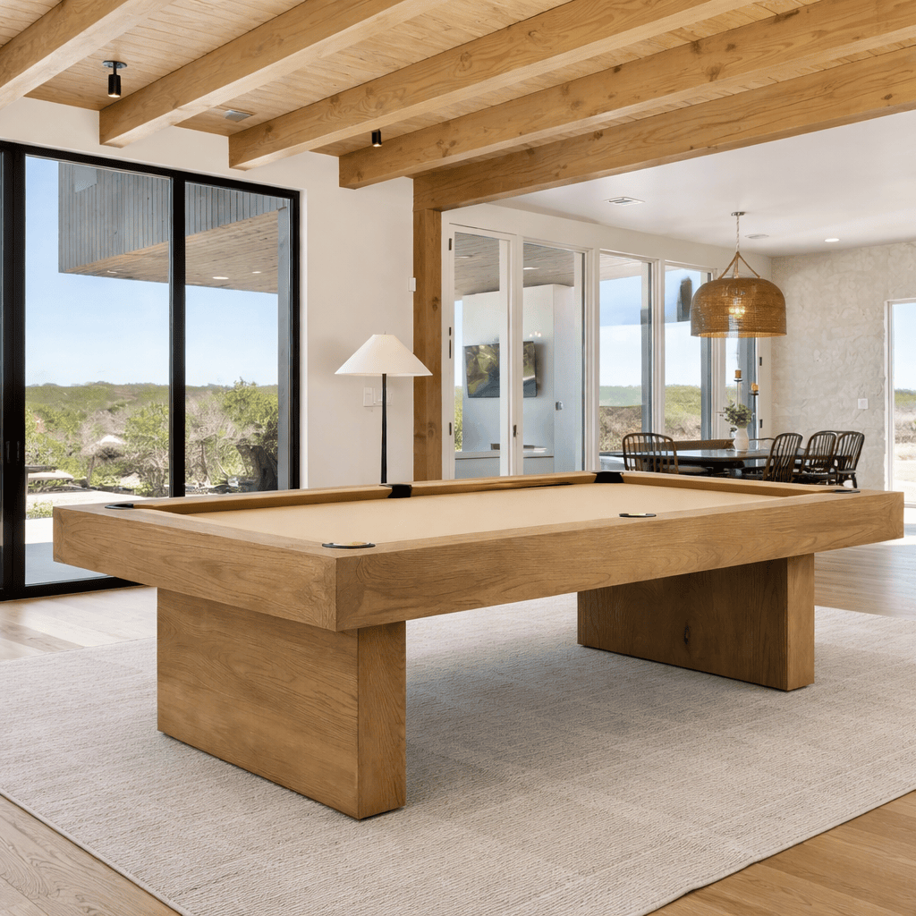 Modern wood pool table centered in a spacious home game room with large windows, an open floor plan, dining area, and surrounding room for comfortable play. Learn how to choose the right pool table by considering table size, room dimensions, playing clearance, construction, and style.